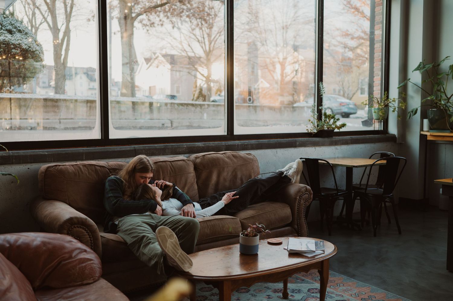 Couple sharing an intimate moment near large windows in dramatic lighting.