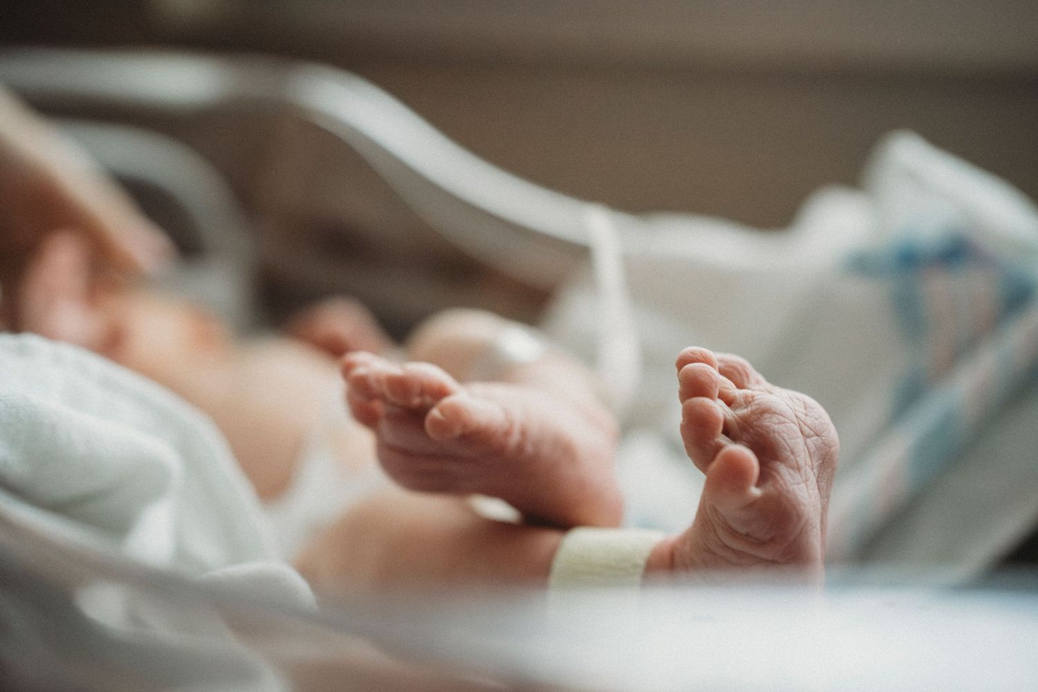 Close up of tiny newborn baby feet on white hospital bedding.