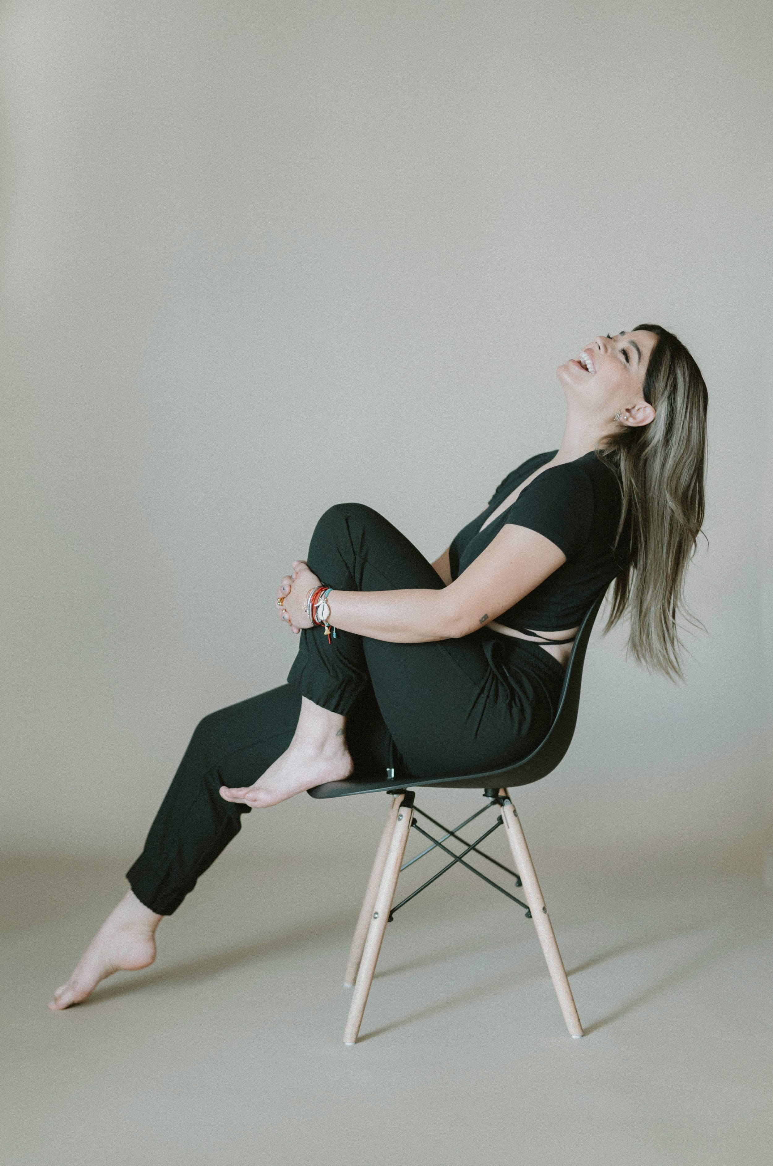 Woman in black outfit laughing while sitting casually on modern chair.