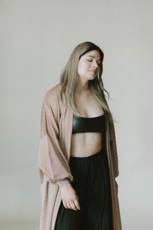 Fashion portrait featuring cozy pink cardigan over black activewear set against minimal studio backdrop.