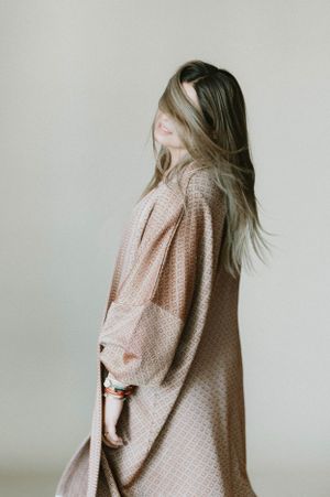 Side profile of long-haired model in oversized knit cardigan against minimalist backdrop.