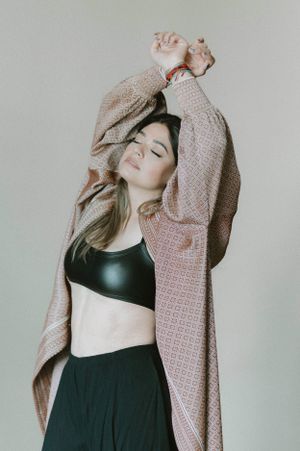 Joyful pose with arms raised wearing pink cardigan and black athletic wear in studio setting.