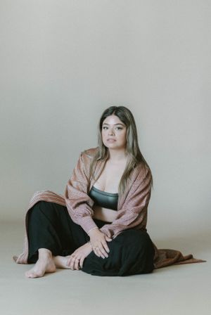Seated portrait in comfortable loungewear featuring pink cardigan and black separates against neutral backdrop.