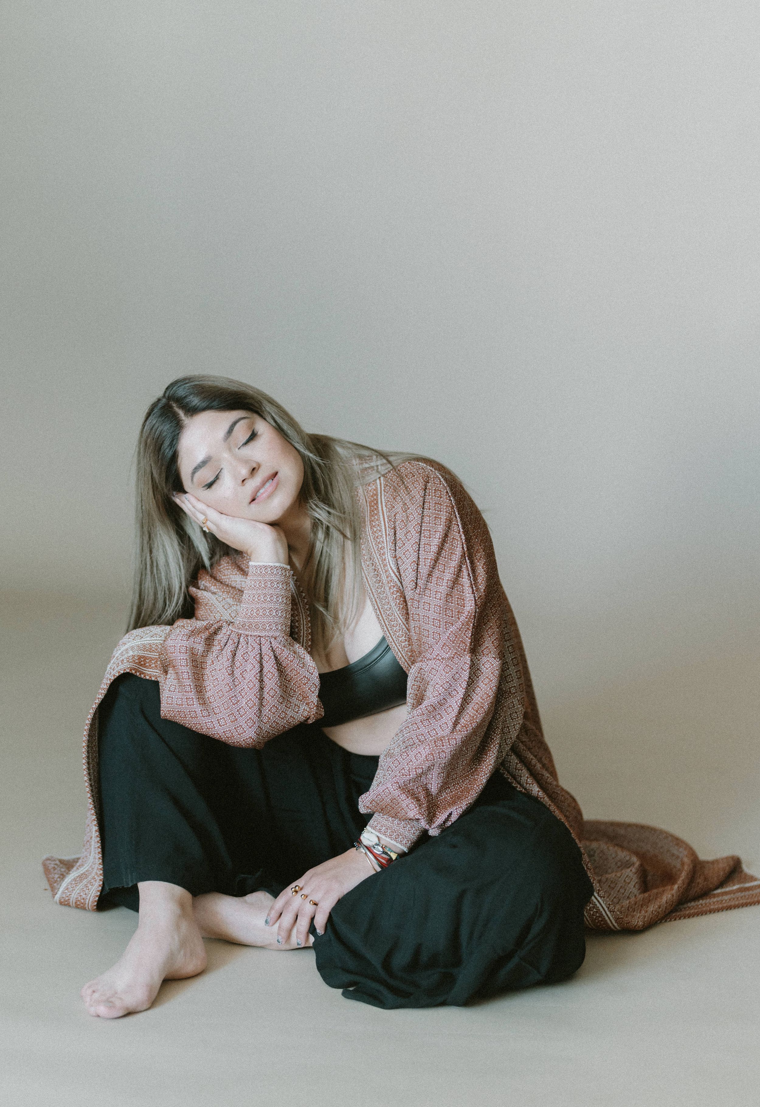 A person in a cozy pink sweater and dark pants relaxes in a minimalist setting with soft lighting.