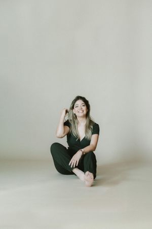 Playful studio portrait of woman sitting cross-legged on floor.
