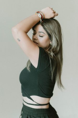 Fashion portrait of woman in black crop top with bracelets against neutral backdrop.