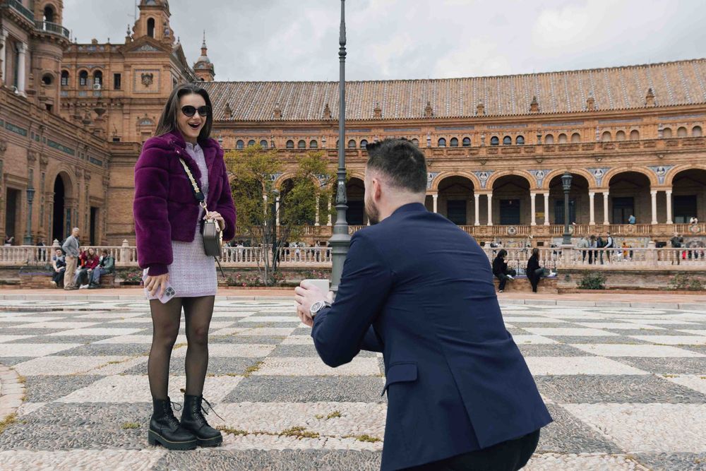 Couple shares romantic proposal moment in front of Plaza de España's iconic architecture.