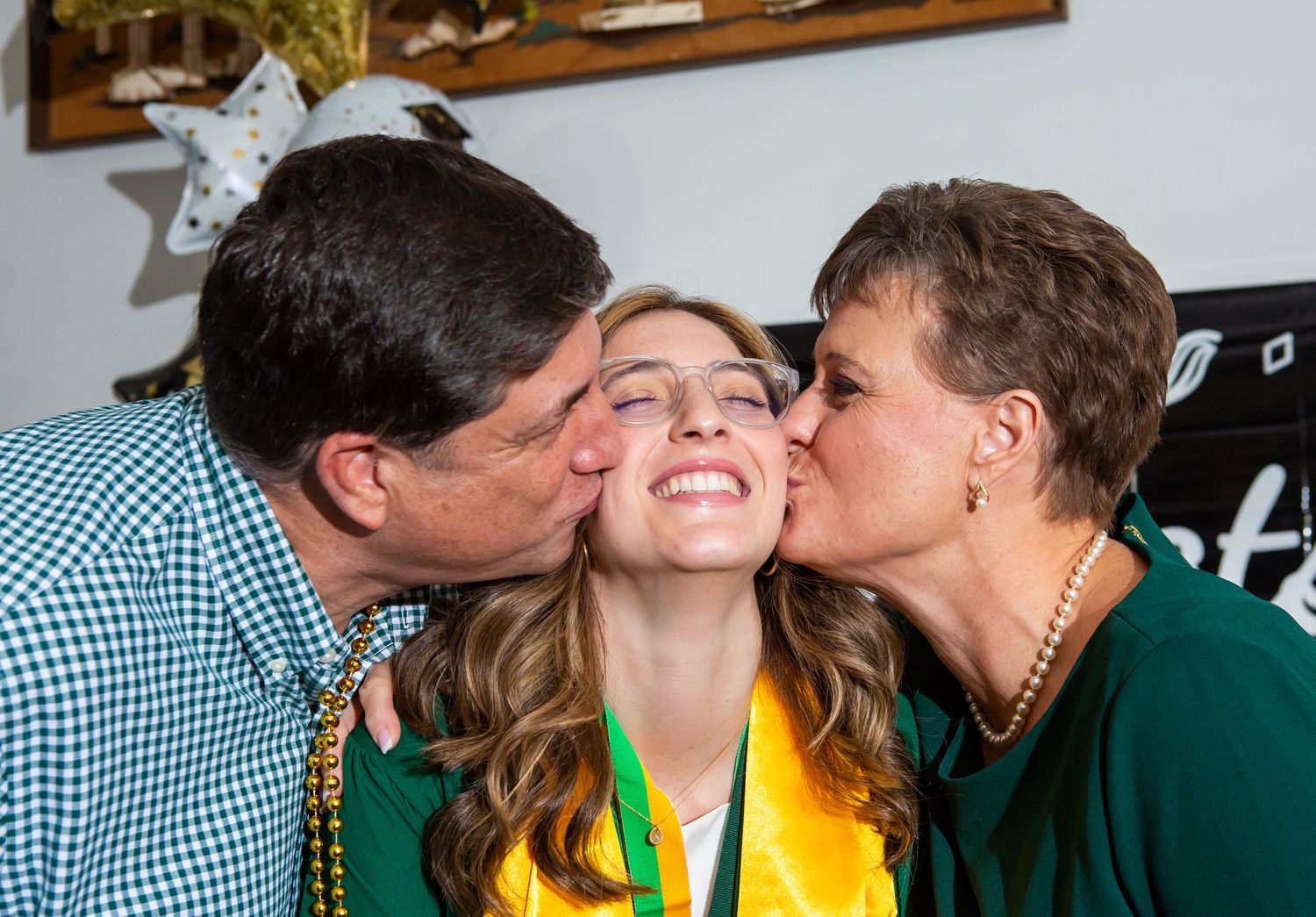 mom and dad kissing their daughter at graduation party.