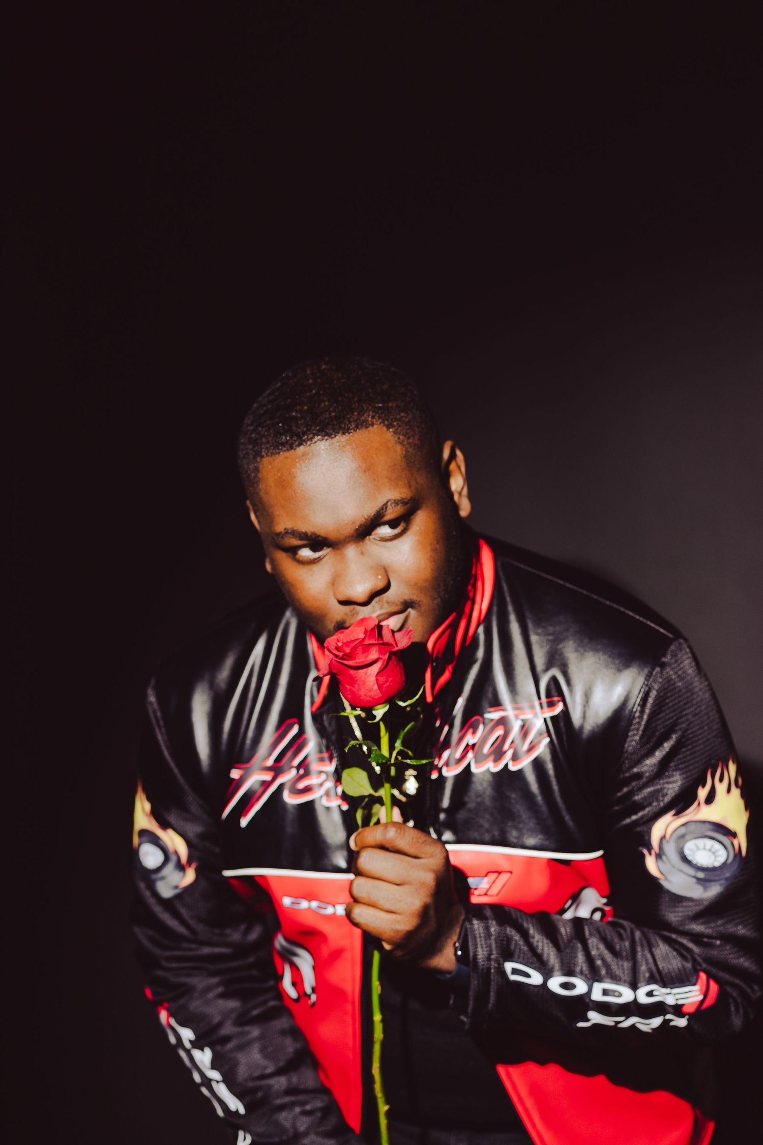 Dramatic portrait showcasing a person in leather jacket holding red rose against dark background.