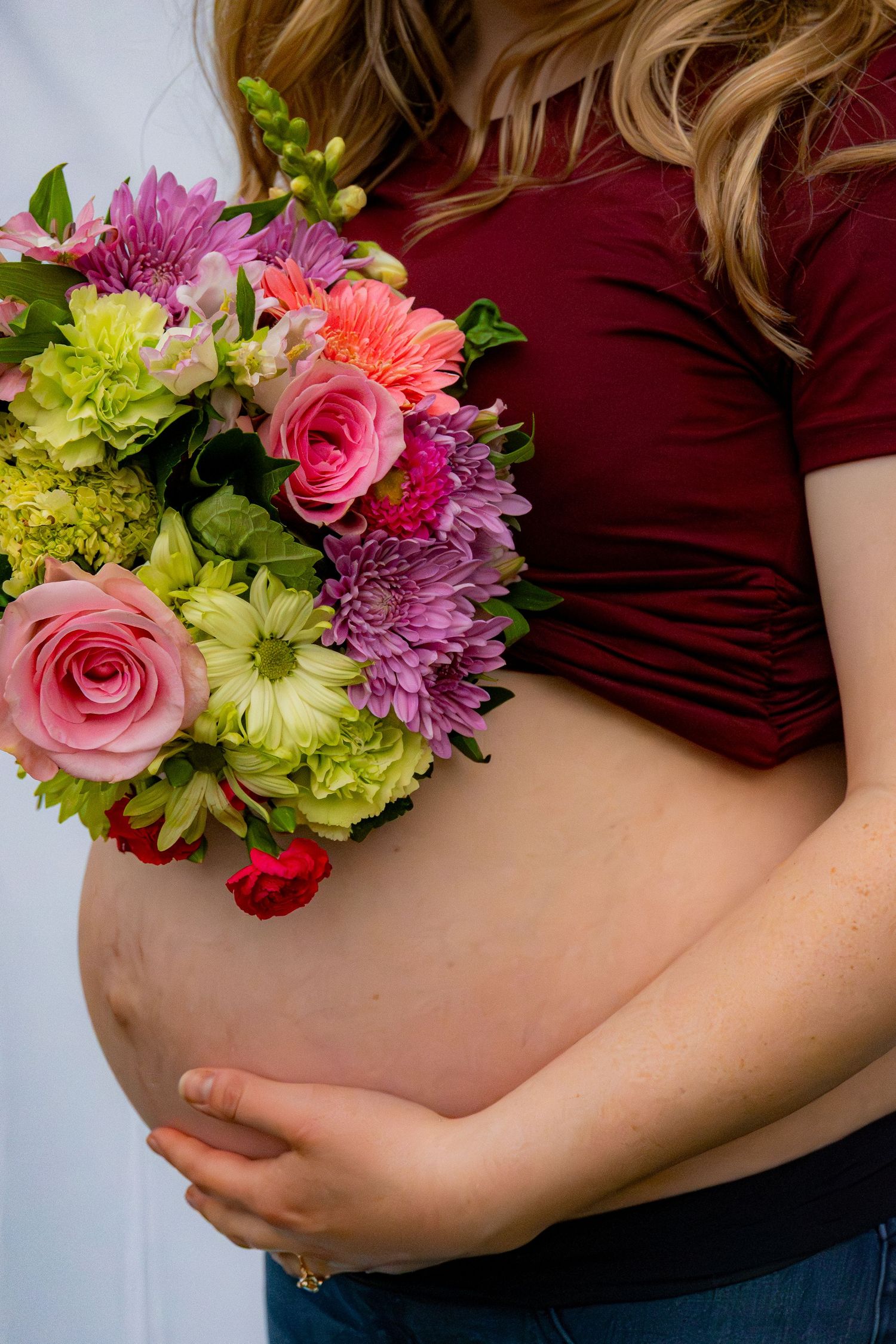 A woman's pregnant belly. She is holding her belly with her left hand and a bouquet of flowers with her right.