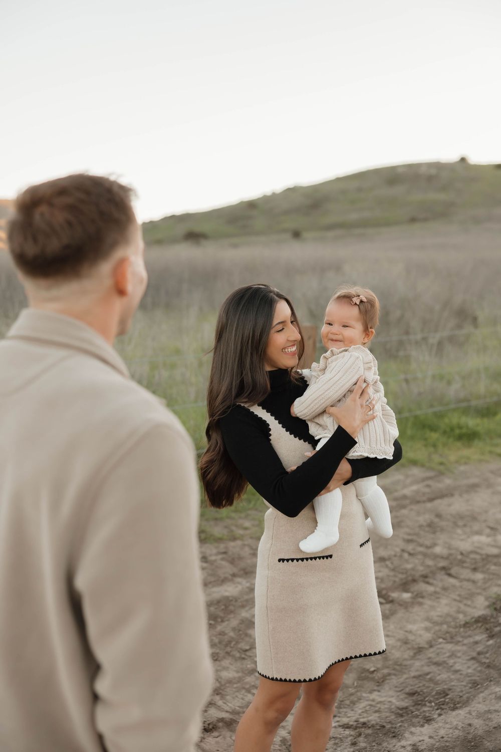 A family shares tender moments in matching cream and black outfits during an outdoor photoshoot on rolling hills.