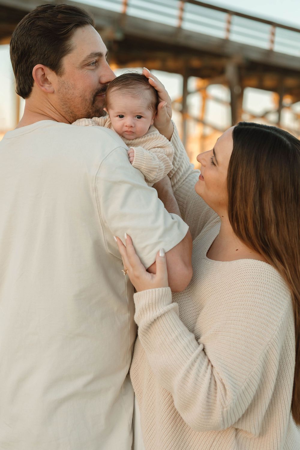 A family shares an intimate moment together outdoors at sunset, wearing matching cream-colored sweaters.