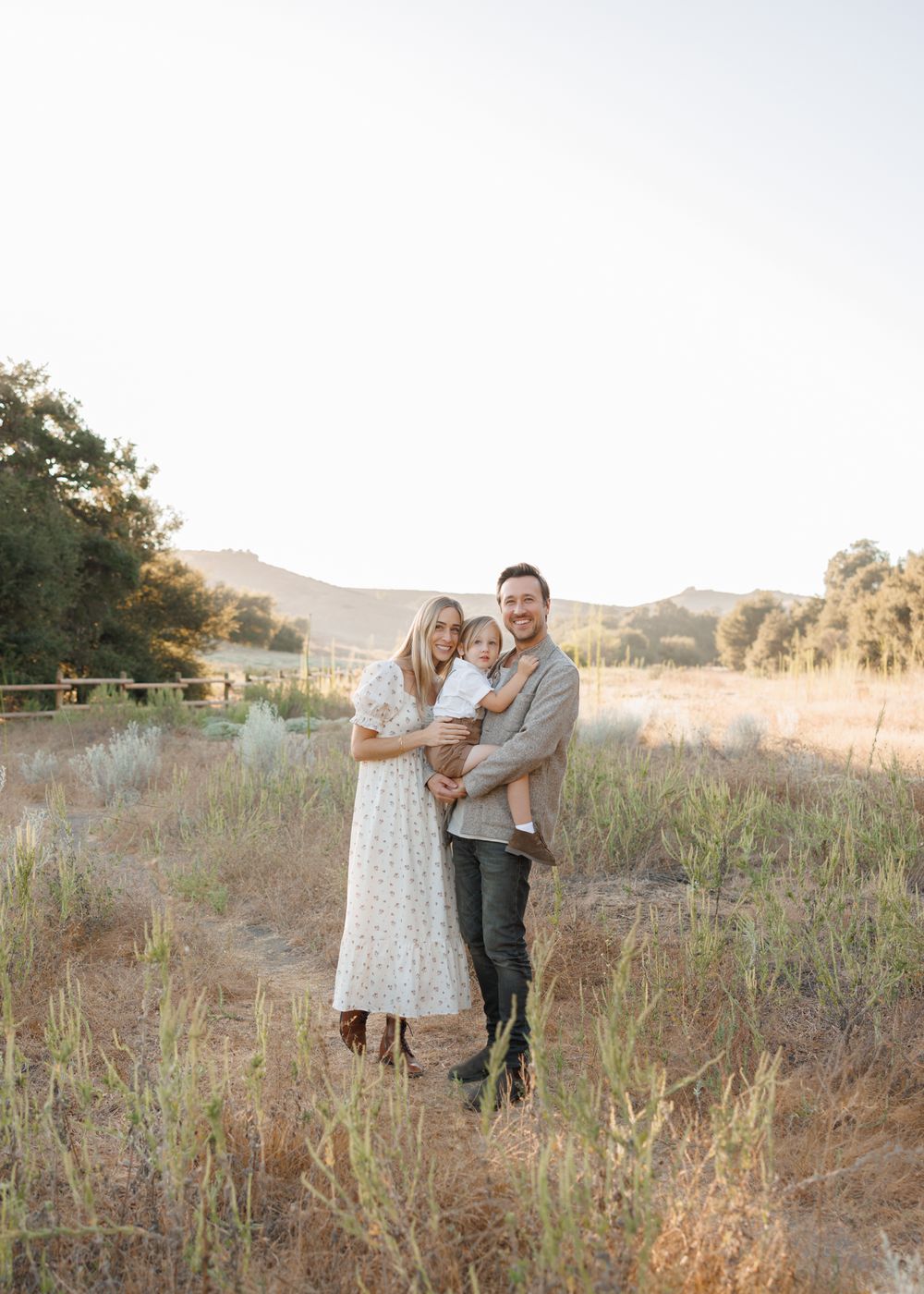 A family portrait in a golden field at sunset with mountains in the background.
