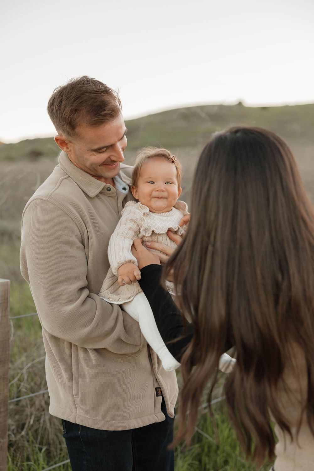 A family shares tender moments together in a grassy field during a sunset photoshoot.