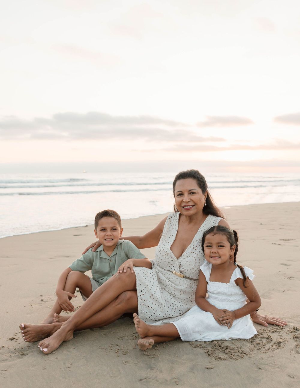 Family members lying together on sandy beach at sunset creating candid moments by the ocean waves.