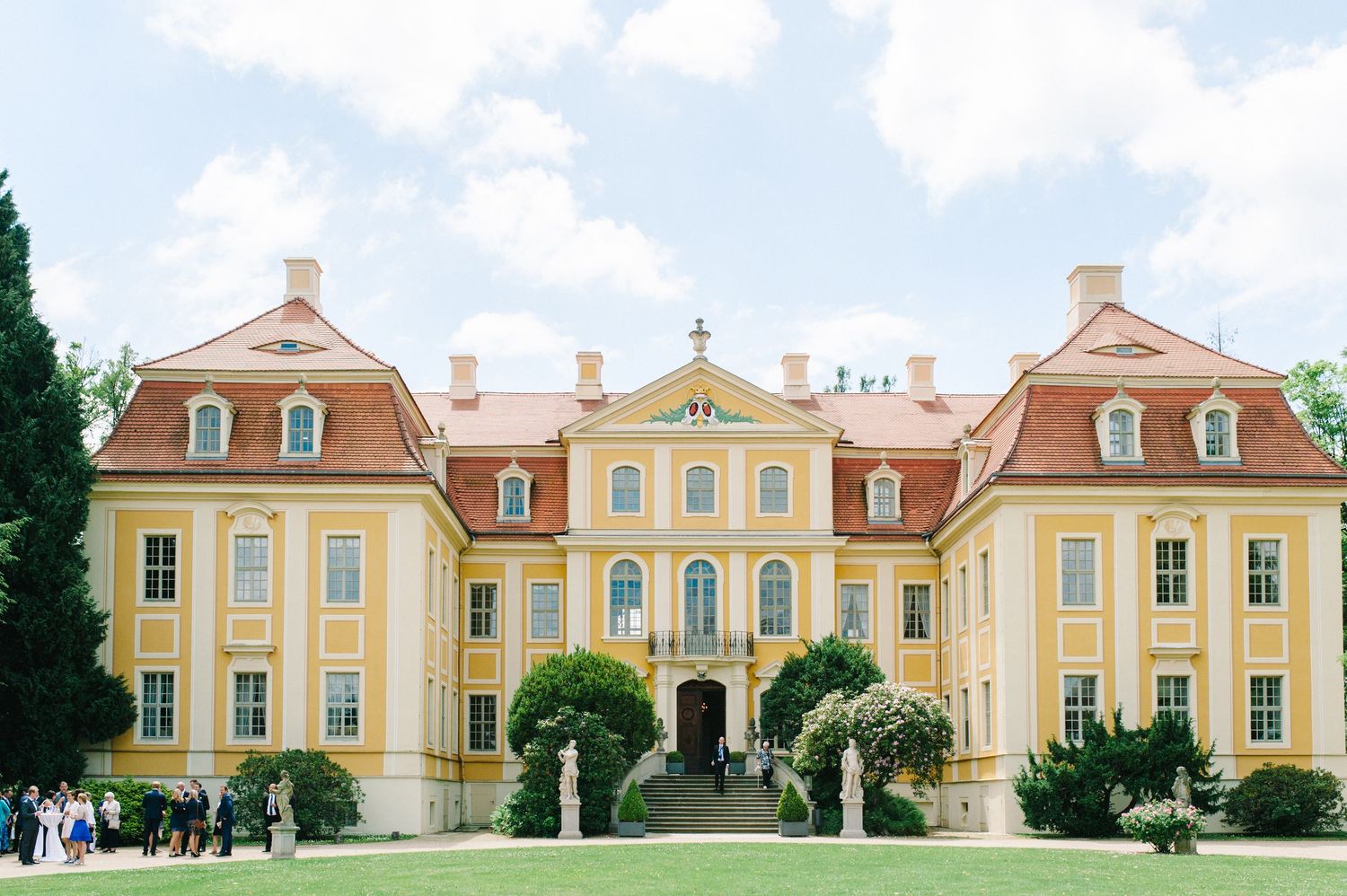 Row of colorful baroque buildings with pastel yellow and peach facades under blue sky. Organized wedding by MyCastleWedding | Dresden.