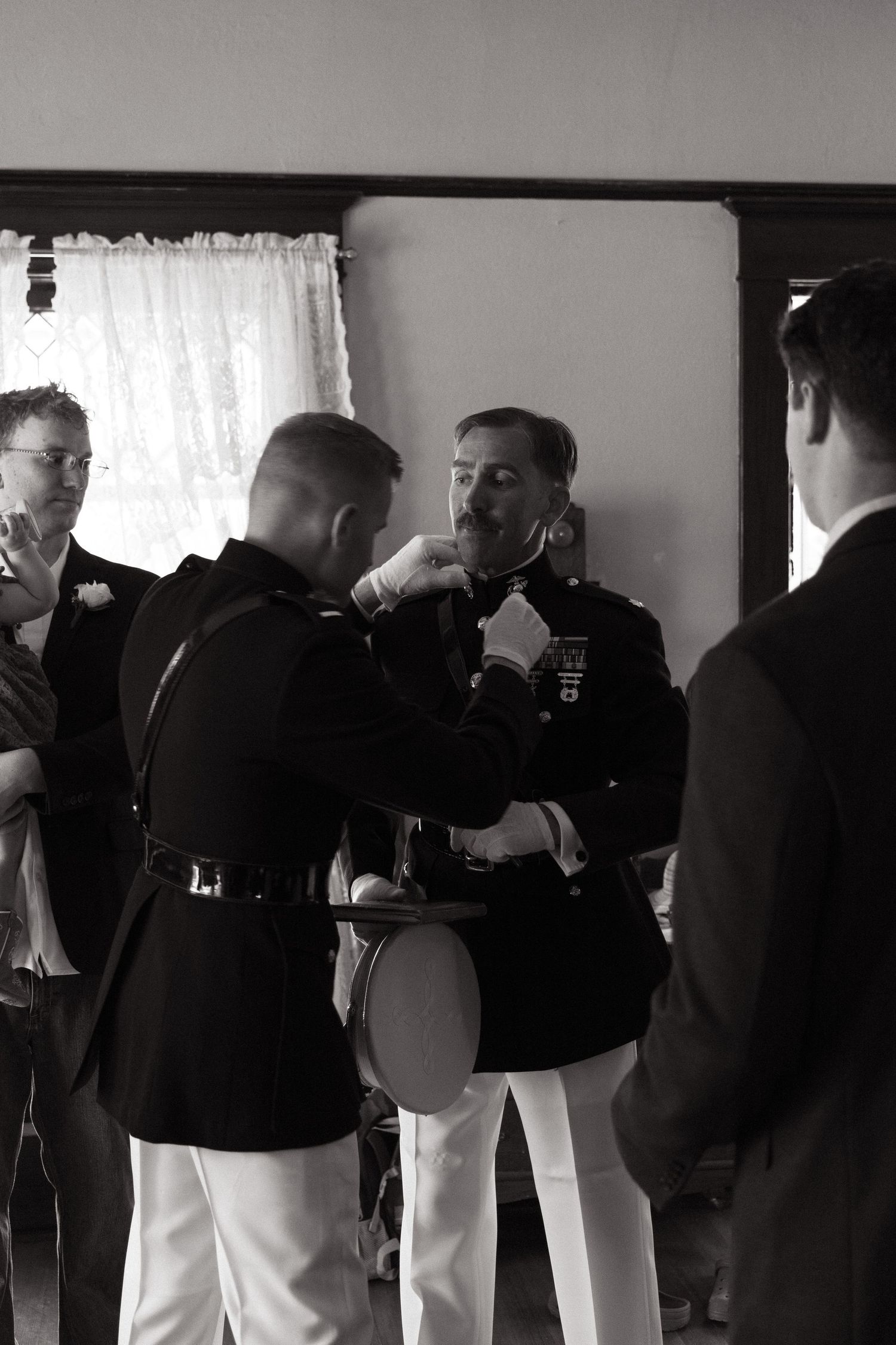 Military groomsmen helping with formal attire preparations in black and white.