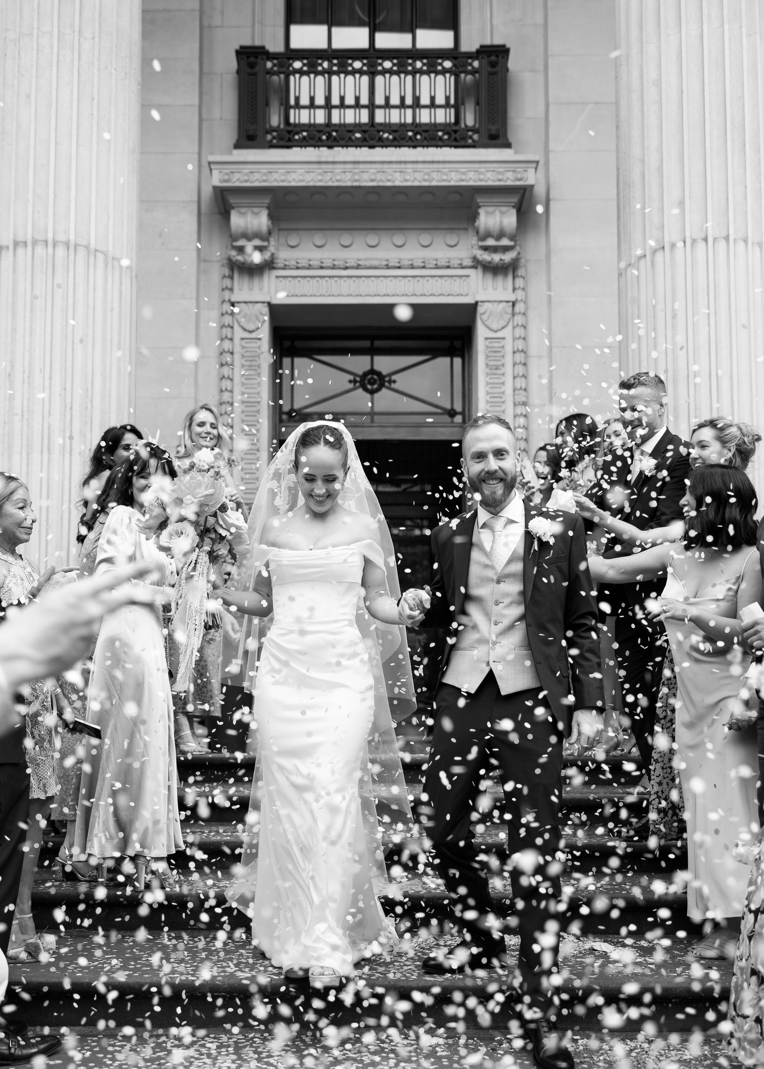 Wedding couple celebrating with guests throwing confetti outside a building with classical columns at a London wedding.