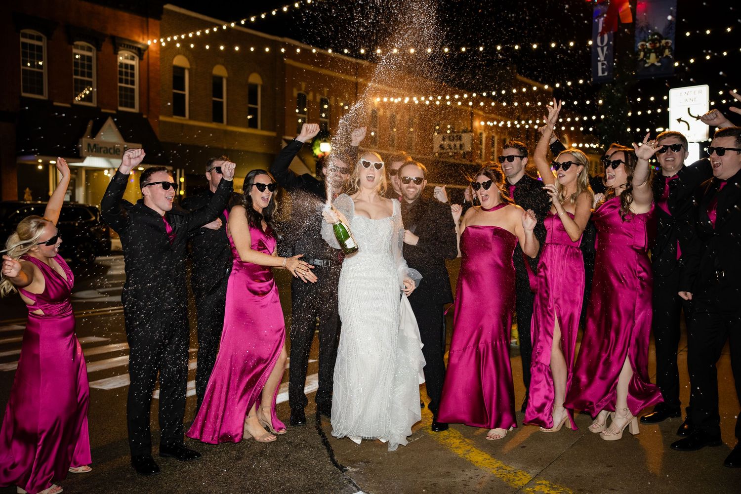 Wedding party dancing under string lights at an outdoor evening reception.