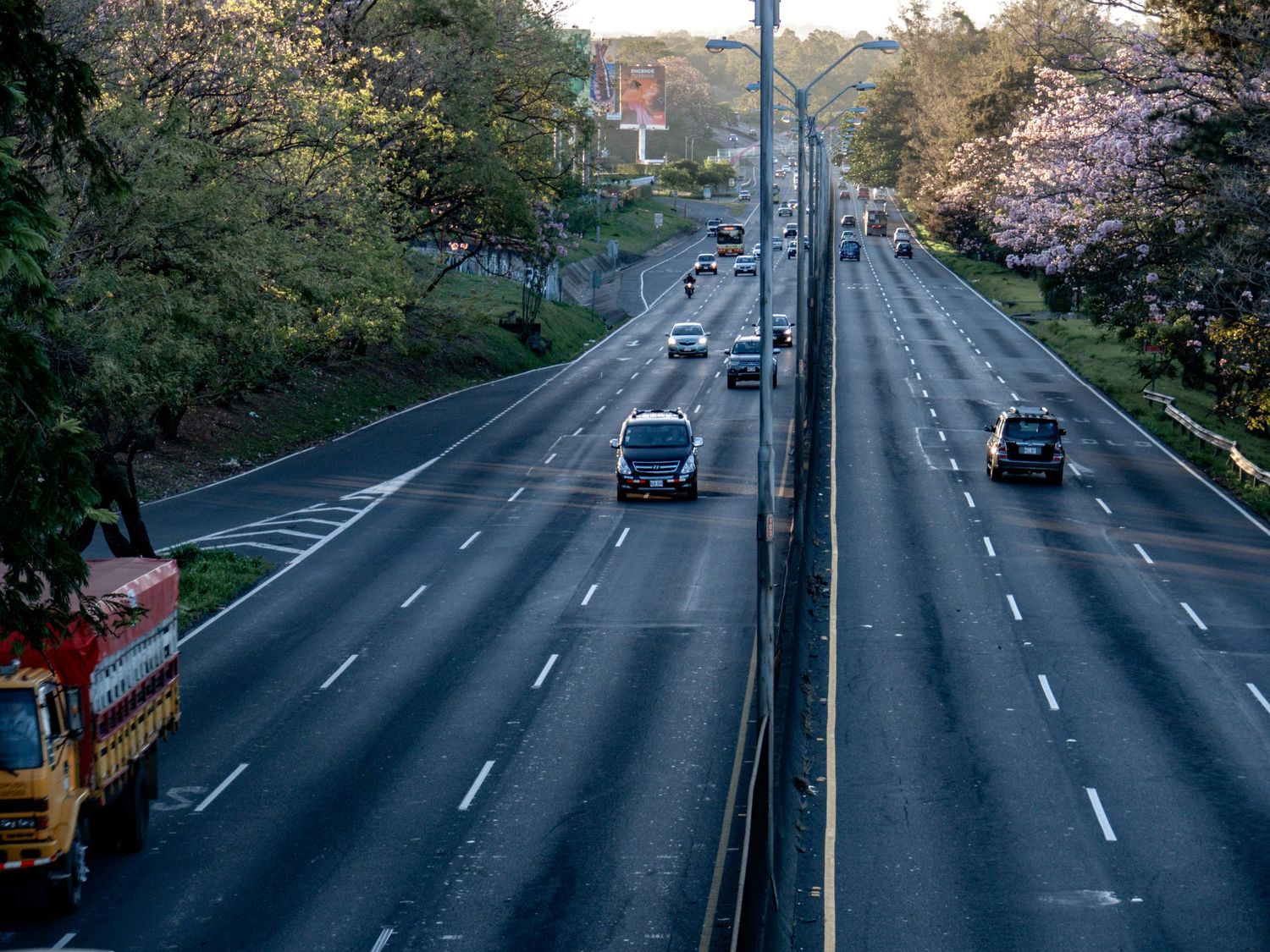 Aerial view of a multi-lane highway with sparse traffic and trees lining both sides.