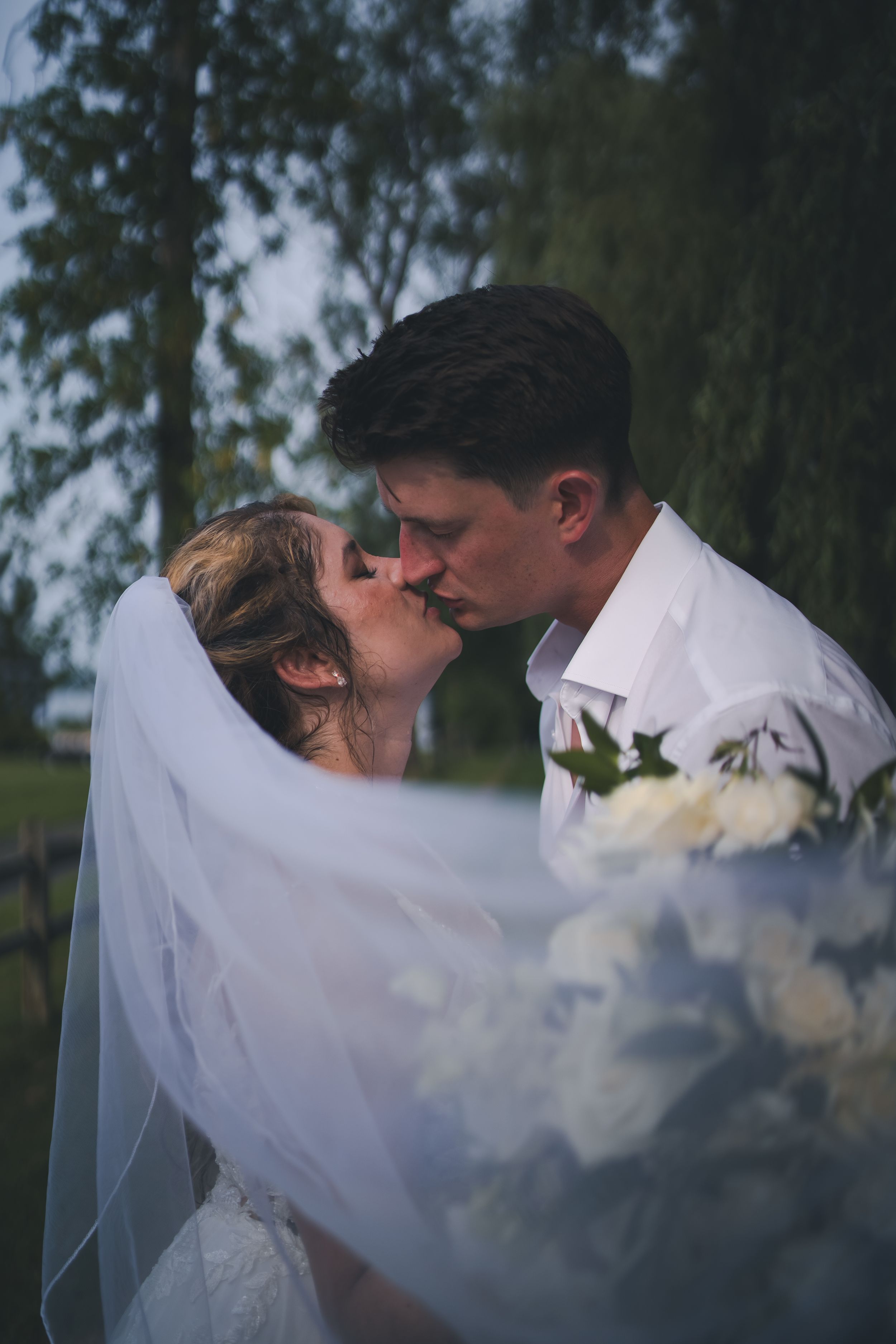 Intimate wedding kiss moment with flowing veil and white floral details.