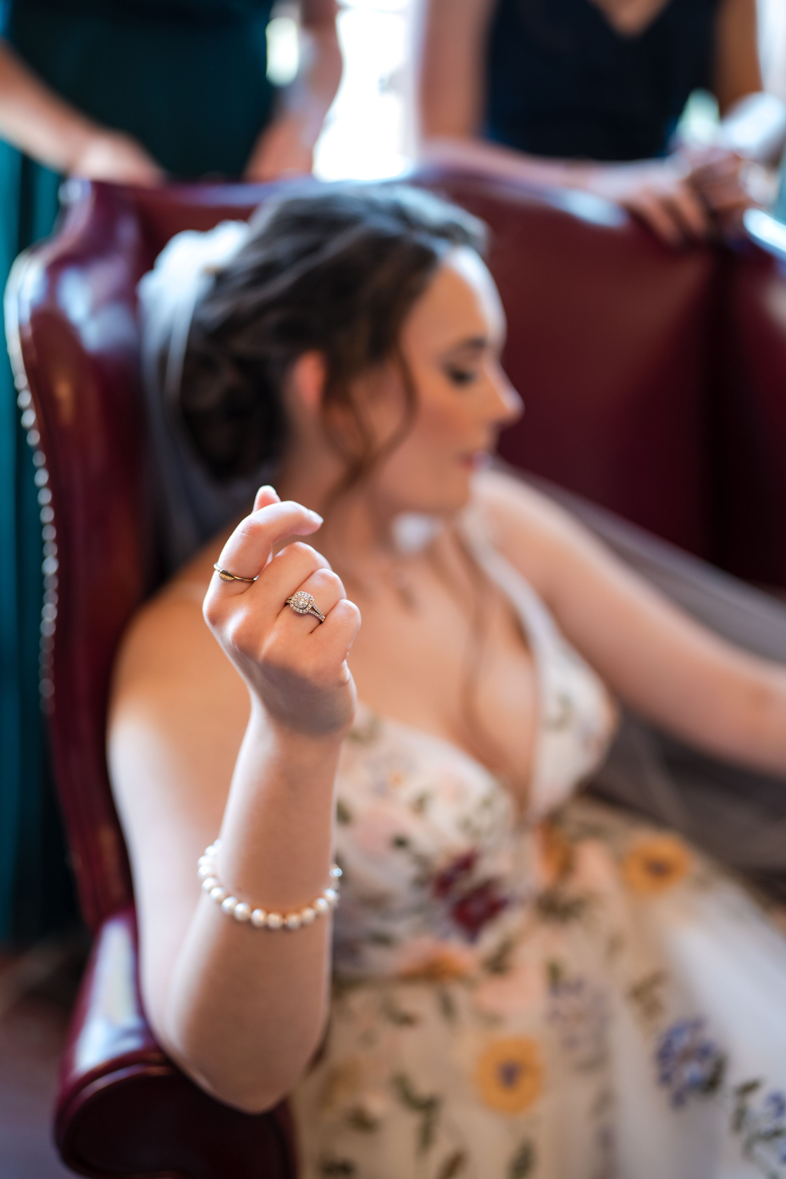 Close-up of a pearl bracelet and engagement ring on a bride's wrist as she sits in a floral dress.