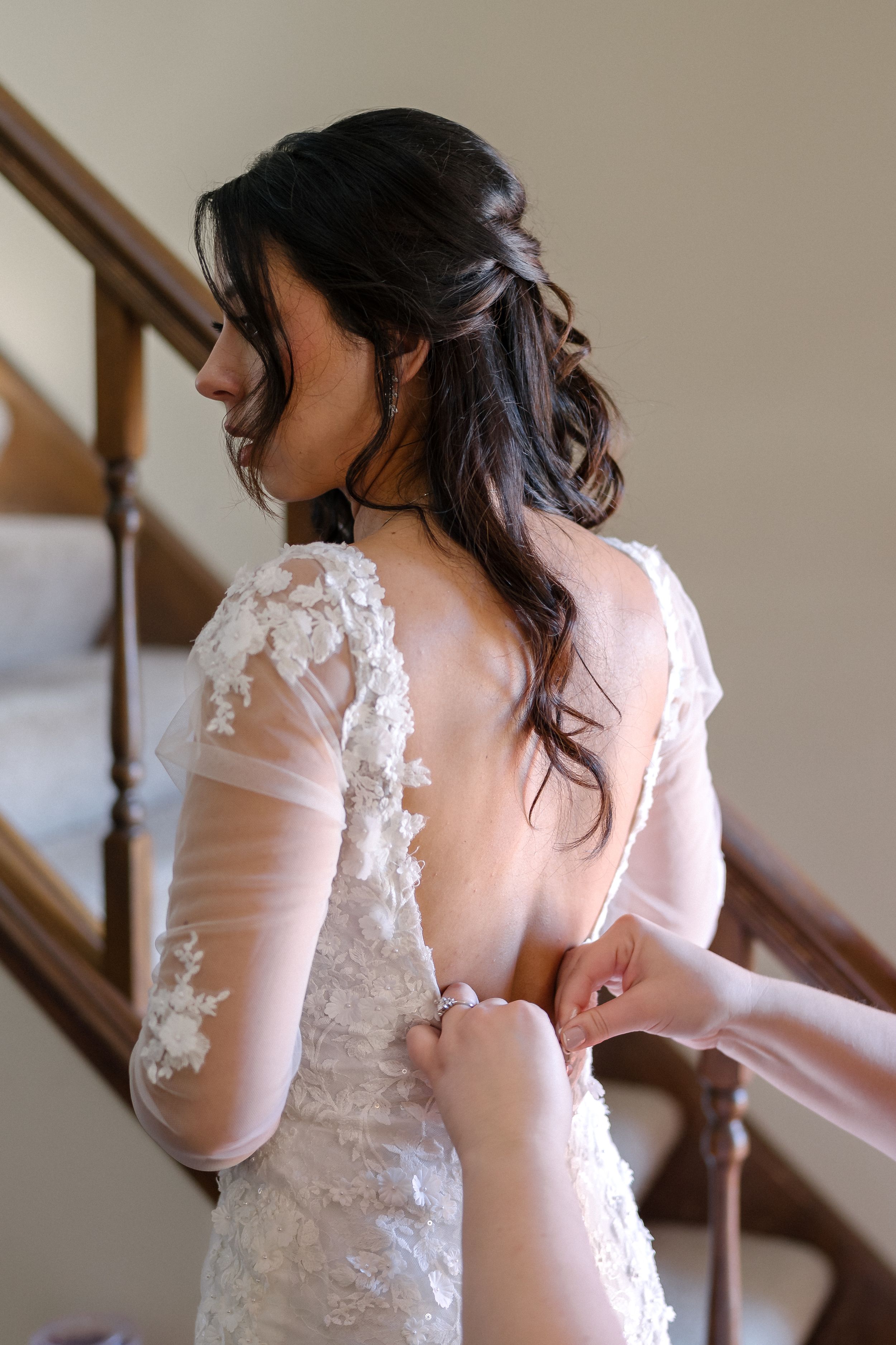 Back view of a wedding dress with delicate lace appliques and sheer long sleeves on a staircase.