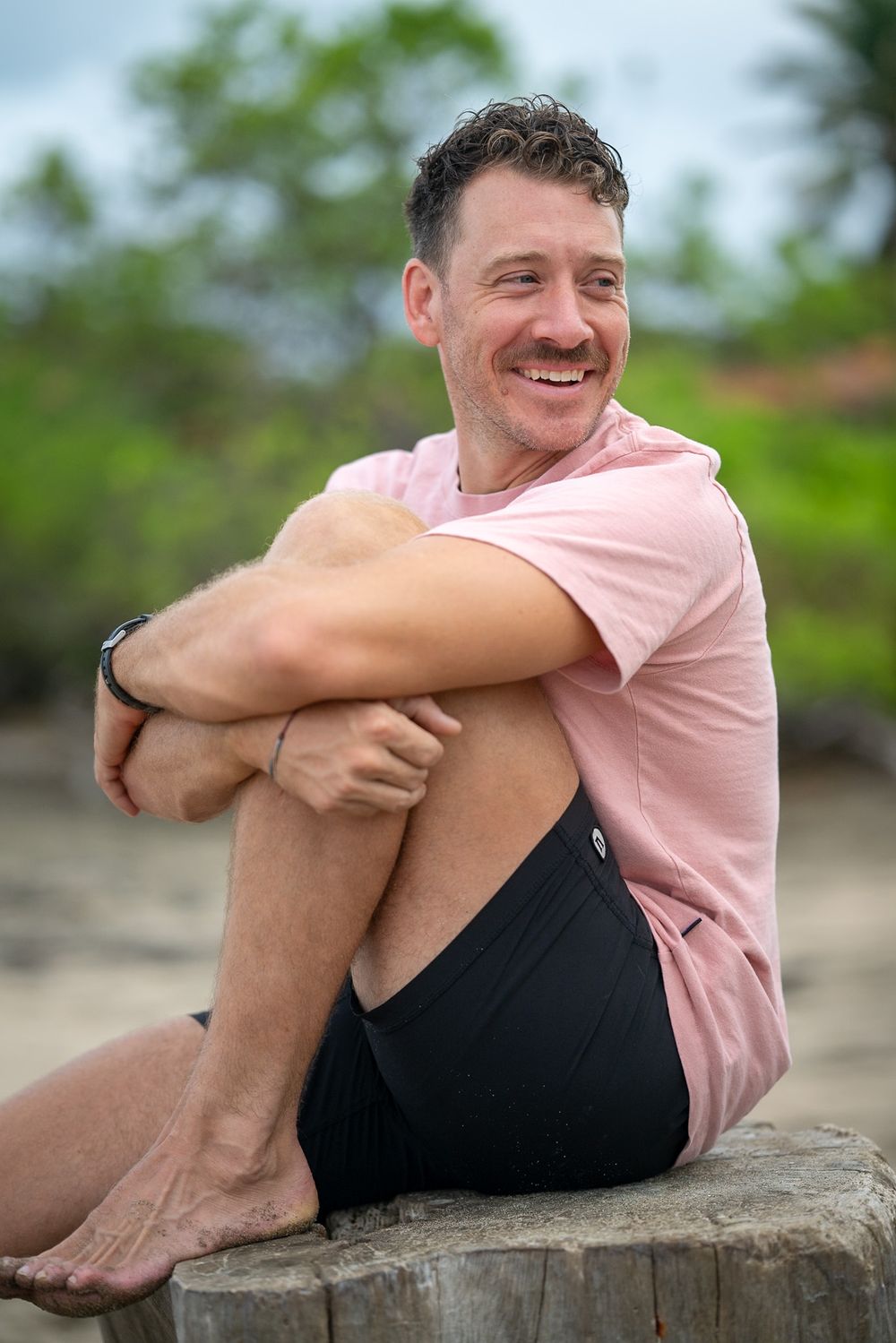 Person sitting casually on driftwood at the beach.