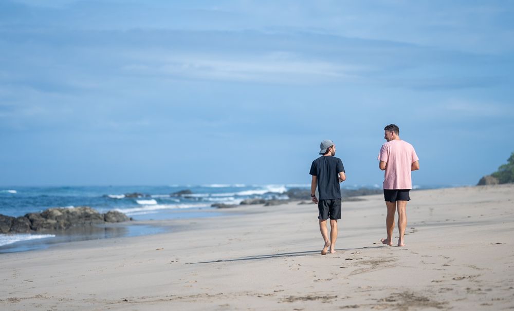 Two individuals walking along a scenic beach with waves crashing in the background.
