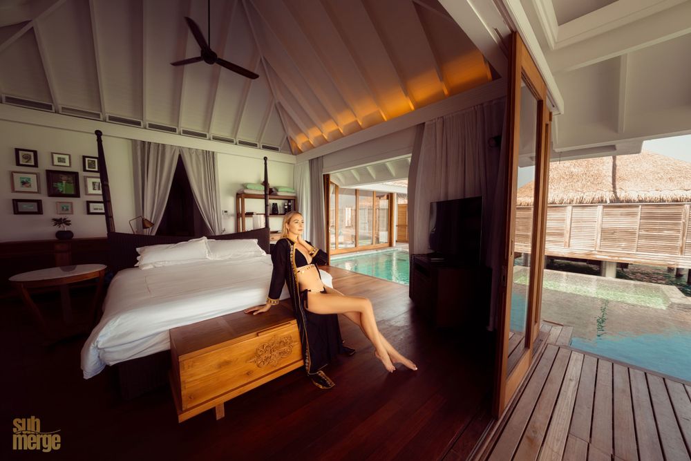 Modern overwater villa bedroom interior with sliding doors opening to private deck and lagoon view.