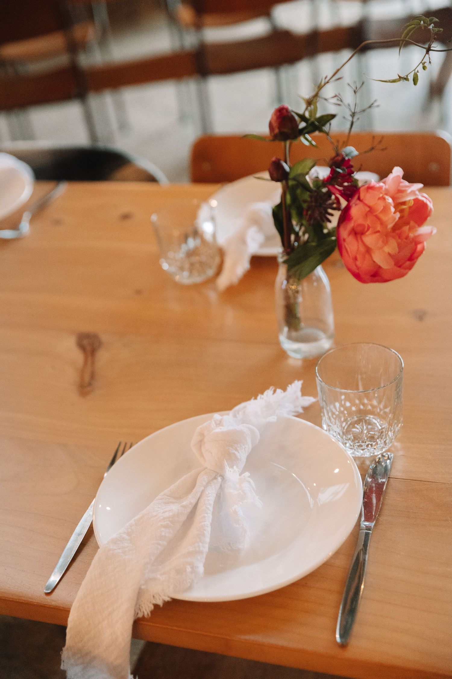 Elegant place setting with white napkin and coral flower centerpiece on wooden table.