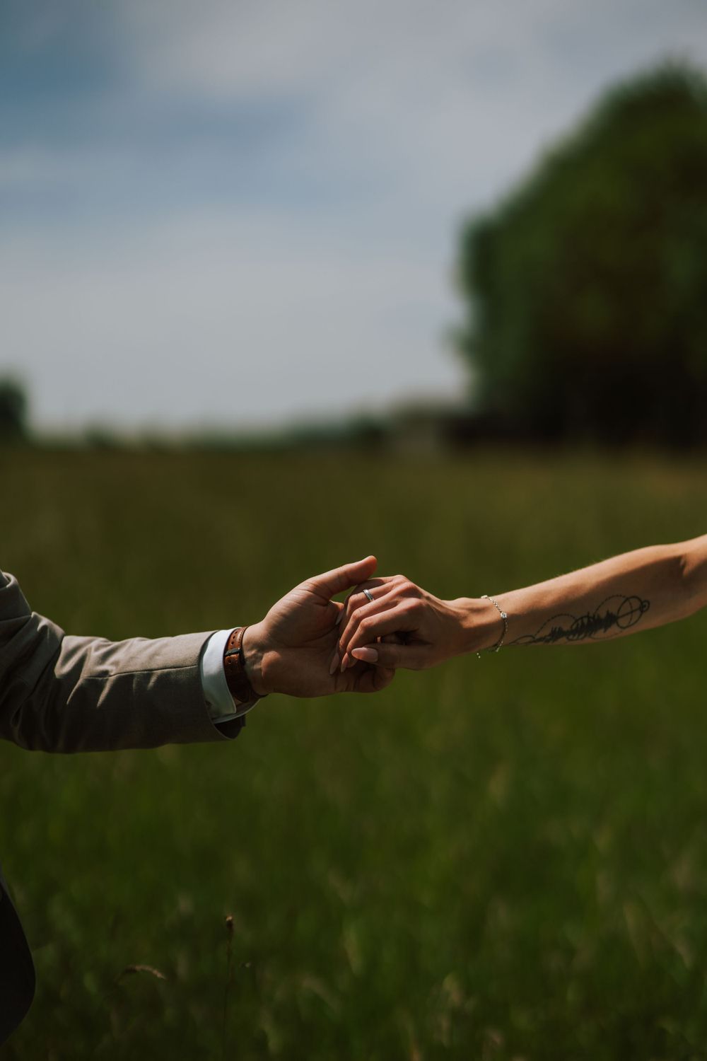 Two hands reaching towards each other against a blurred green field background.