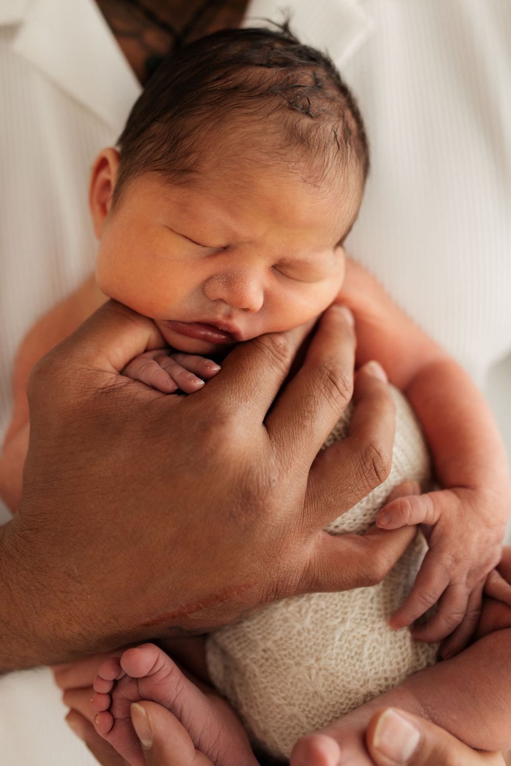Close-up of hands cradling a peaceful sleeping newborn baby.