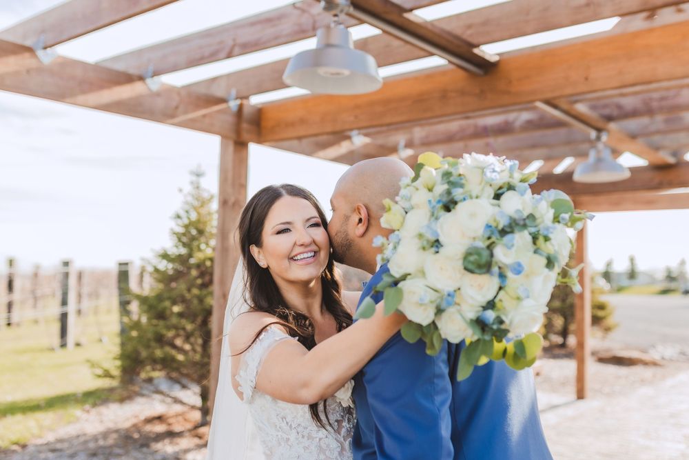 A joyful moment on a sunny day under a wooden pergola with a large white and blue floral bouquet.