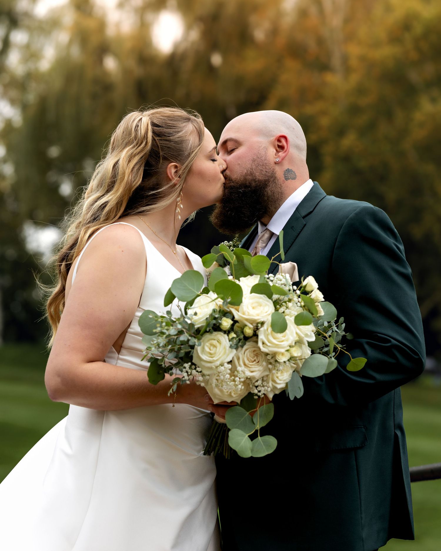Bride and groom sharing romantic kiss under wedding veil with colorful bridal bouquet in foreground.