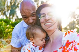 A joyful family portrait outdoors with sunlight streaming through trees in the background.