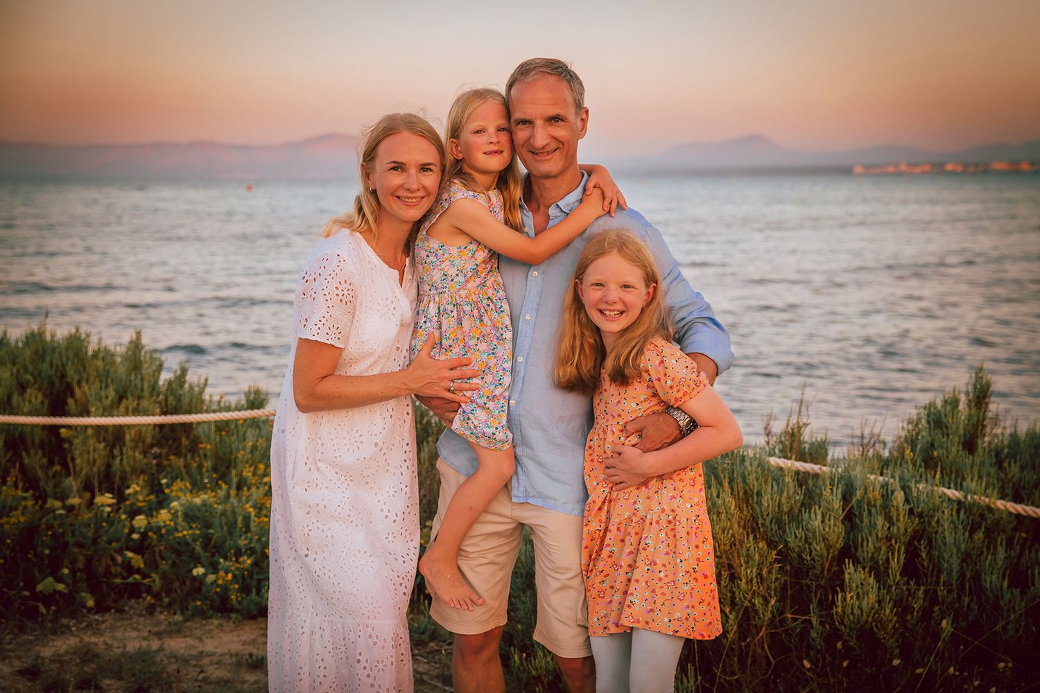 A happy family  of four standing near the ocean during golden hour.