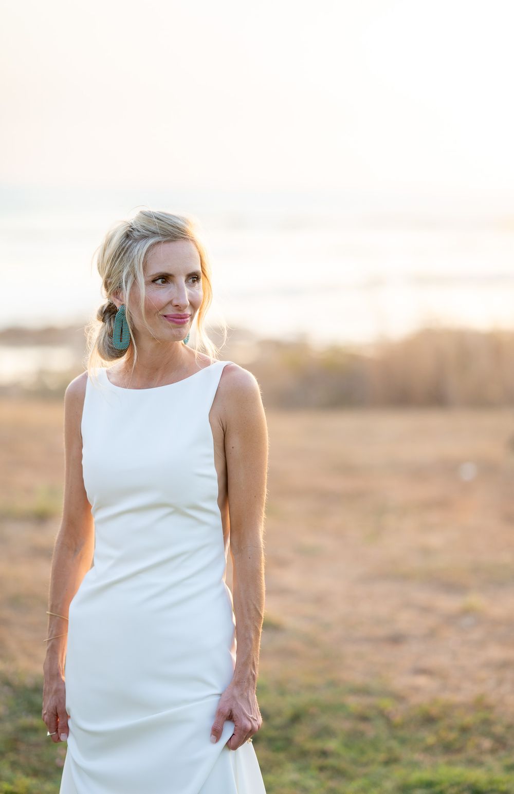Elegant bride in white dress poses at sunset on beach.