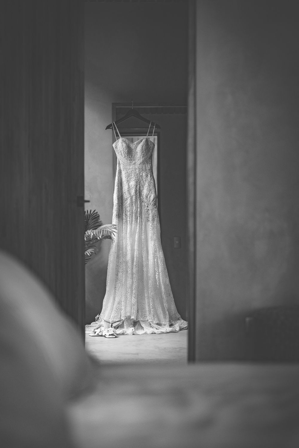 Elegant white wedding dress hanging in doorway, captured in black and white photography.
