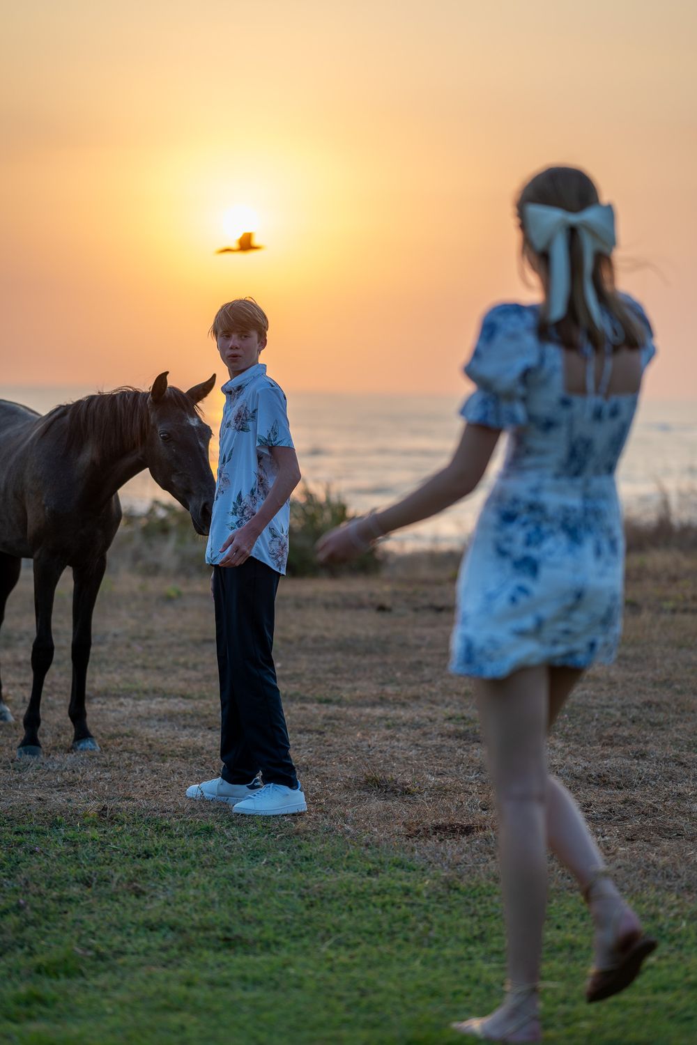 Silhouette of horse and people against orange sunset by the ocean.