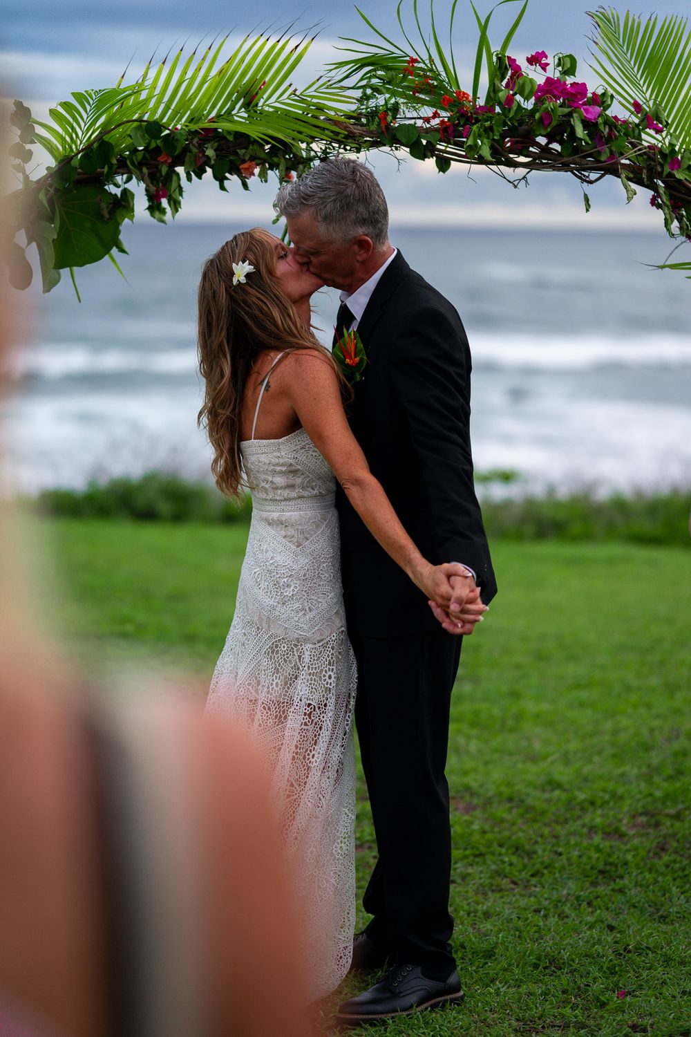 A romantic kiss under a tropical floral arch against an ocean backdrop.