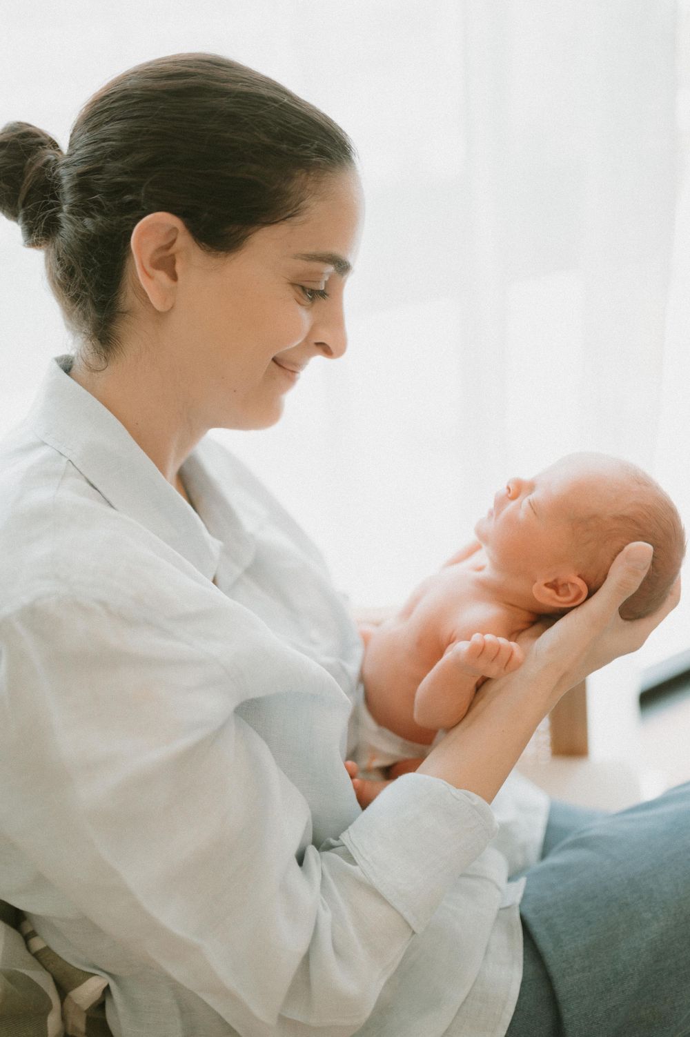 Tender moment between parent and newborn baby in morning light by window.