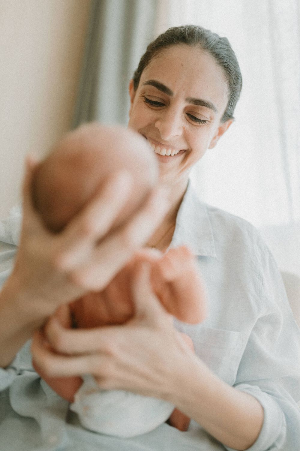 Parent in white shirt holding and gazing lovingly at newborn baby near window.