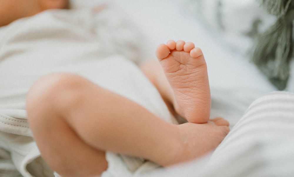 Close up of baby's tiny foot against white bedding.