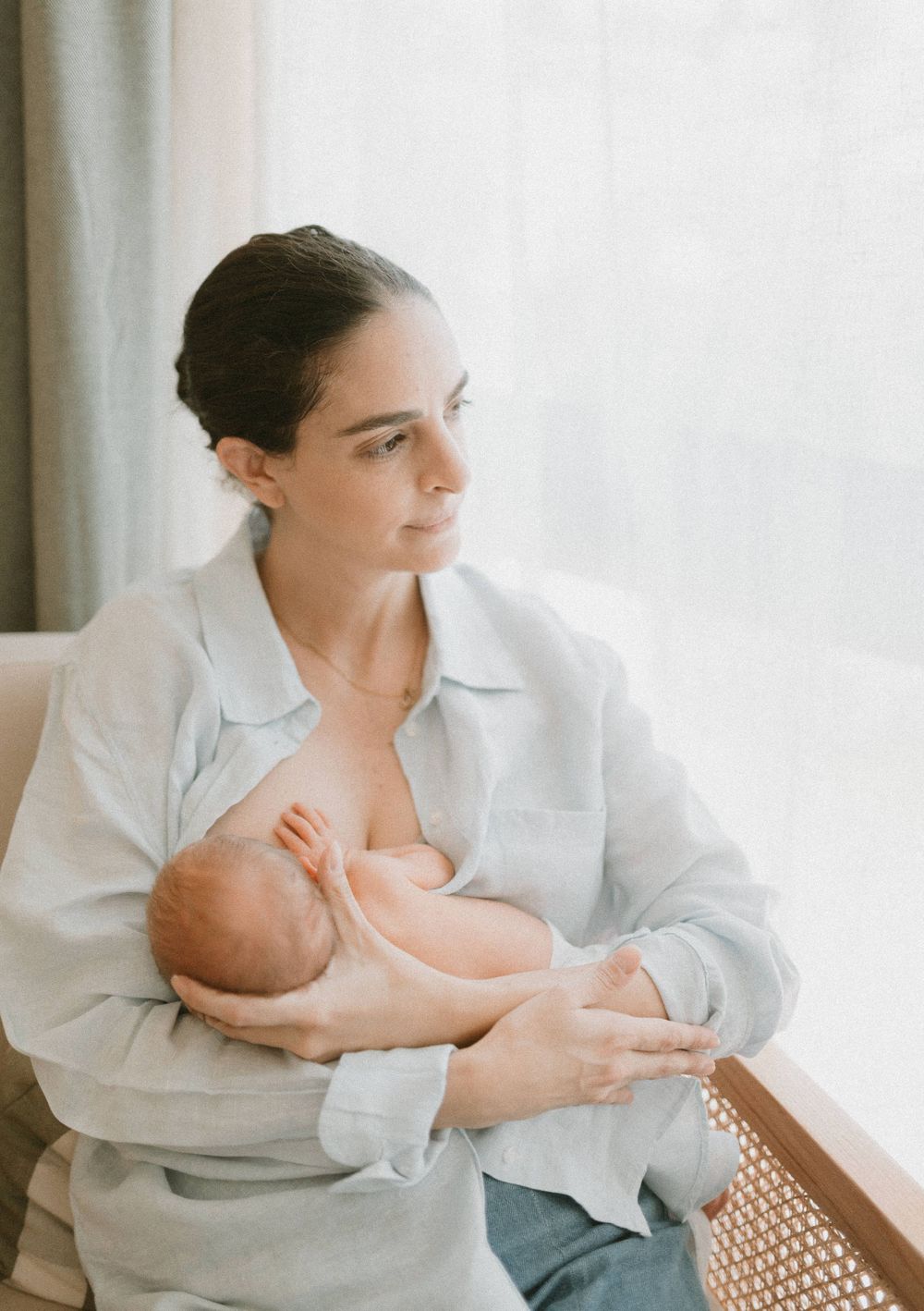 Parent in white button-down shirt nursing newborn baby in natural window light.