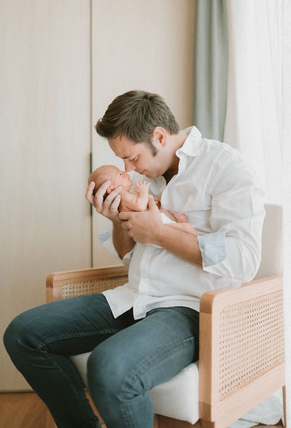 Parent in white shirt tenderly holding newborn baby in rattan chair.