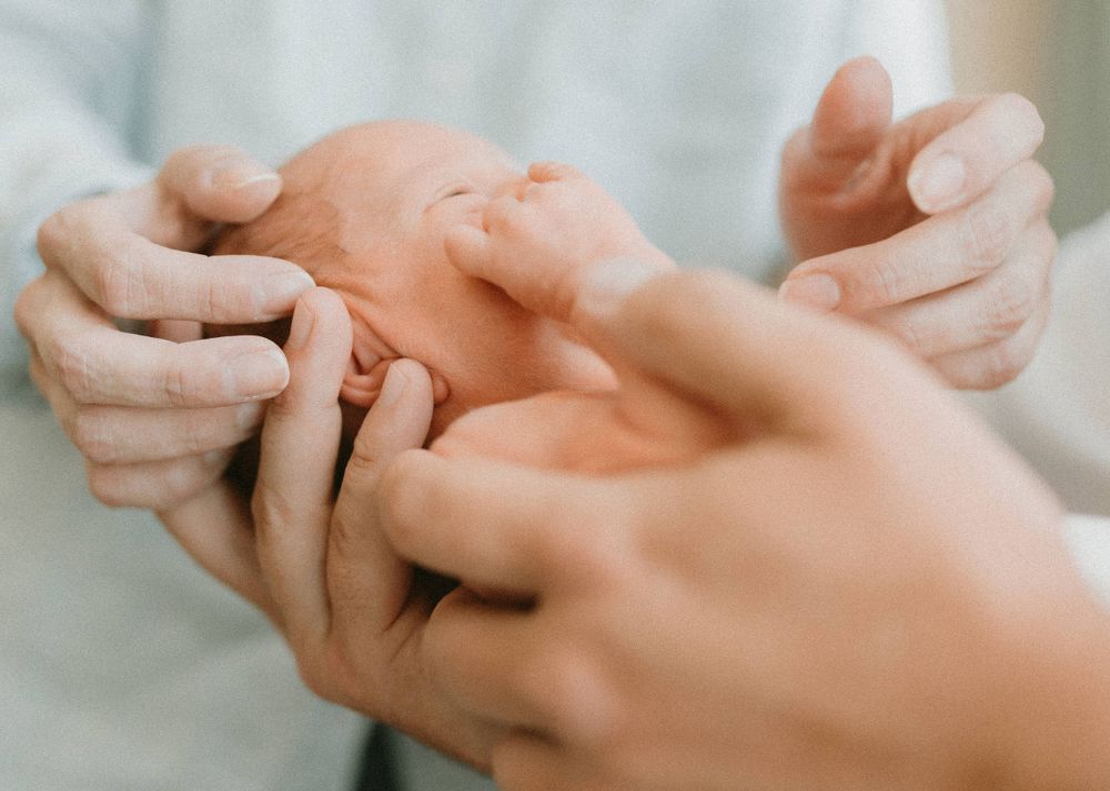 Gentle hands cradle and support a newborn baby during a tender moment.