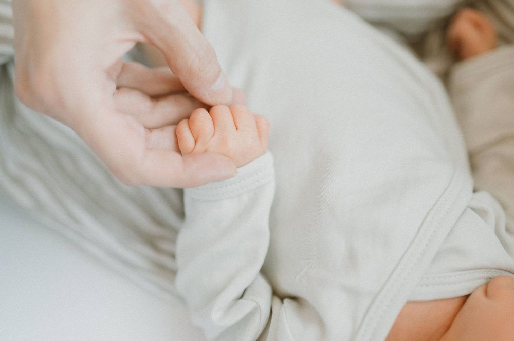 Gentle close-up of adult hand holding baby's tiny fingers.