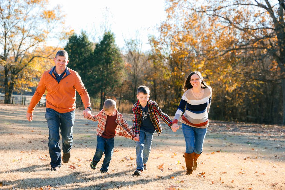 Family holds hands while running together on dirt path during autumn season.