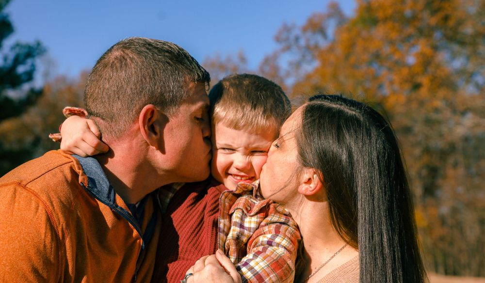 An intimate family moment sharing kisses and laughter together on a sunny fall day.